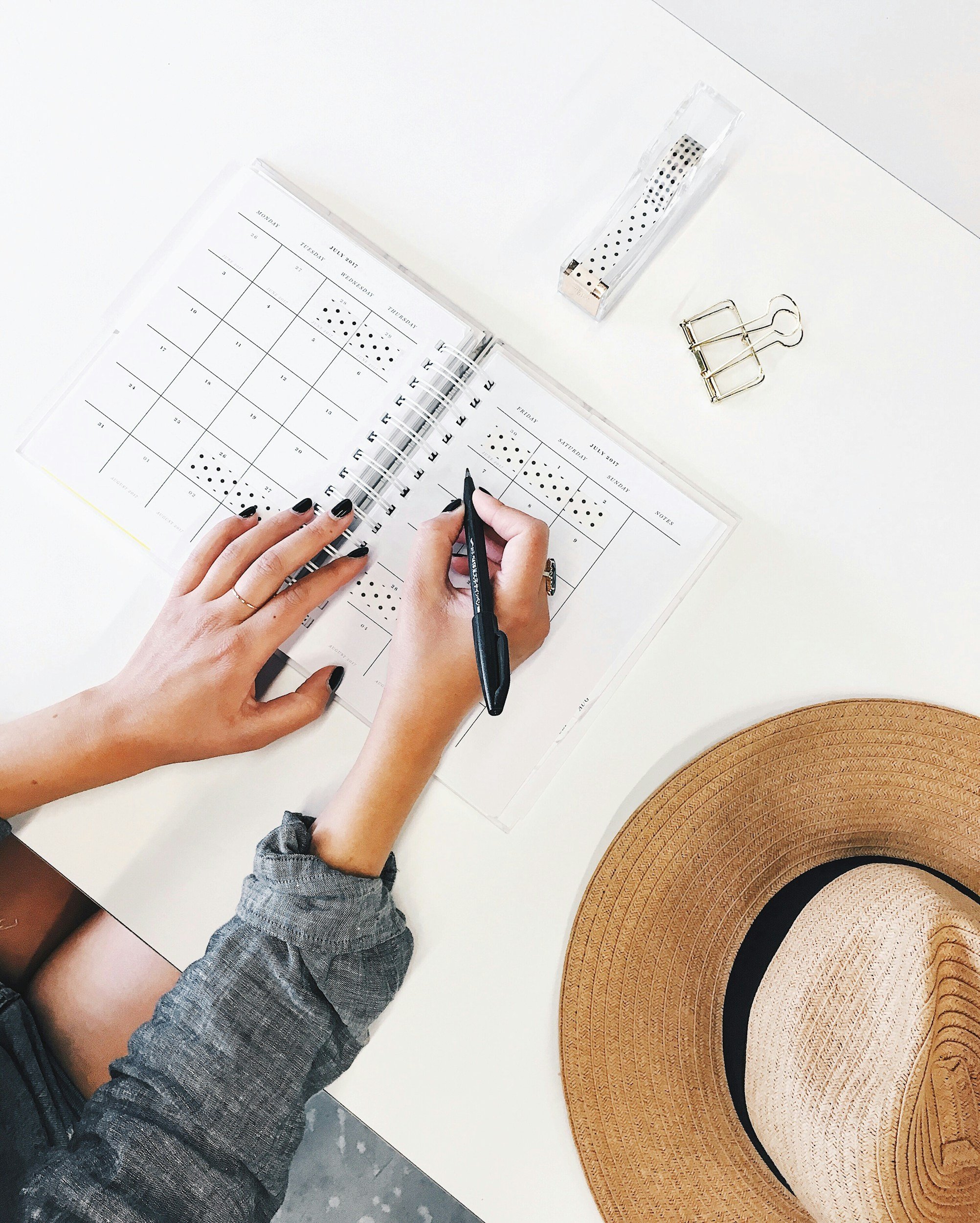 Manicured hands writing in a planner with a pen on a white desk surface